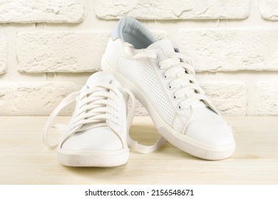 Pair Of White Sneakers On White Brick Background. Unisex Shoes, Stylish White Sneakers.