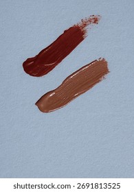 A pair of smudges—beige-red and maroon—on a white surface.