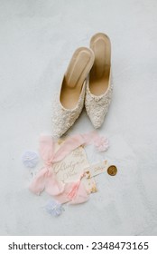 a pair of white wedding shoes at white background with  pink ribbon and wedding calligraphy invitations at weddingday