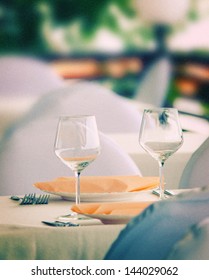 Pair of wineglasses on elegant table setting. Outdoor shot. Toned image, grain added