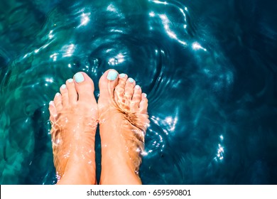 Pair of woman's feet with light blue manicure on blue sea background with white reflections - Powered by Shutterstock