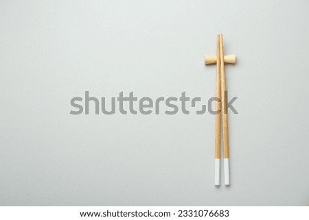 Pair of wooden chopsticks with rest on light grey background, top view. Space for text