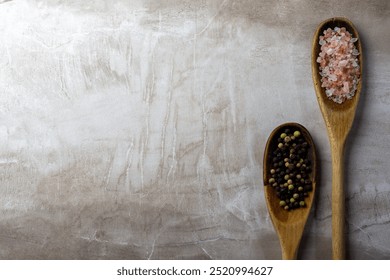 A pair of wooden spoons on a neutral tile background.  Rustic spoons are filled with Himalayan salt and peppercorns.  Copy space. - Powered by Shutterstock