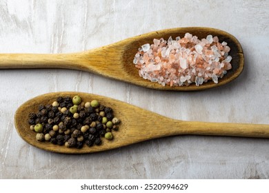 A pair of wooden spoons on a neutral tile background.  Rustic spoons are filled with Himalayan salt and peppercorns. - Powered by Shutterstock