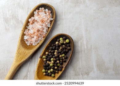 A pair of wooden spoons on a neutral tile background.  Rustic spoons are filled with Himalayan salt and peppercorns.  Copy space. - Powered by Shutterstock