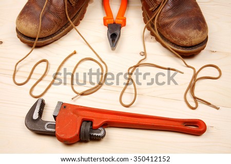 Pair of work boots with red adjustable wrench and pliers. There written the word 'work' by laces on wooden background