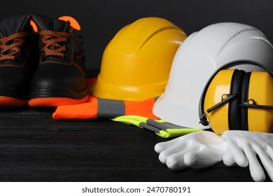 Pair of working boots, hard hats, protective gloves, earmuffs and reflective vests on black wooden surface, closeup - Powered by Shutterstock