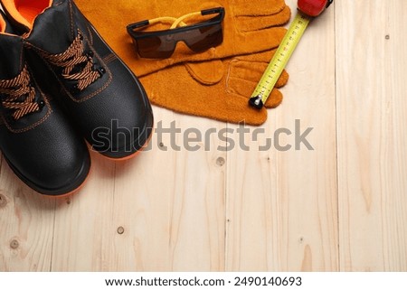 Pair of working boots, protective gloves, goggles and tape measure on wooden background, flat lay. Space for text
