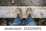 A pair of worn brown work boots stand on a muddy wooden plank, viewed from above.