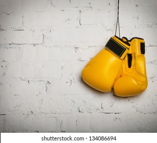 Pair of yellow boxing gloves hanging on a brick wall