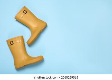 Pair of yellow rubber boots on light blue background, top view. Space for text