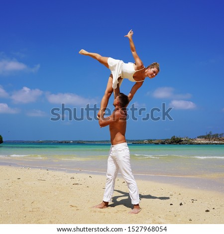 a pair of young flexible acrobats on the ocean posing on the beach.acrobatic elements support on the background of a tropical beach. athletic beautiful couple in white. duo adagio. acrobatic couple