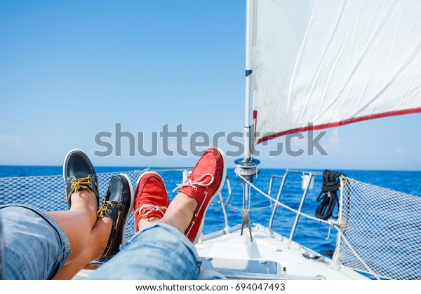 Pairs legs of man and woman legs in red\
and blue topsiders on white yacht deck.\
Yachting