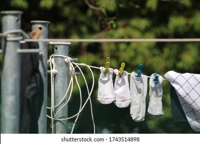 Pairs Of White Ankle Socks With Pegs And A Tea Towel Hanging On A Clothesline With Metal Poles On Blurred Trees Background