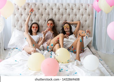 Pajama Party. Attractive Young Smiling Women In Pajamas Drinking Champagne While Having A Slumber Party In The Bedroom