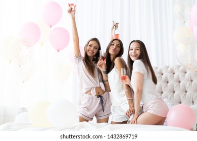 Pajama Party. Attractive Young Smiling Women In Pajamas Drinking Champagne While Having A Slumber Party In The Bedroom