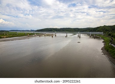 Paju-si, Gyeonggi-do, South Korea - August 9, 2021: High Angle View Of Fishermen Doing Fishing On A Boat On Imjingang River With Muddy Water Against An Iron Bridge
