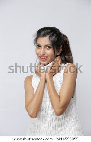 Pakistani Young girl, posing fashionably keeping her hands on her neck , wearing white knitted sleeveless sweater isolated on a white background