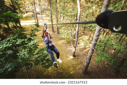 Palanga, Lithuania - 2023: young woman girl sliding along zipline in fir tree forest in summer. Lithuania adventure park in HBH. - Powered by Shutterstock