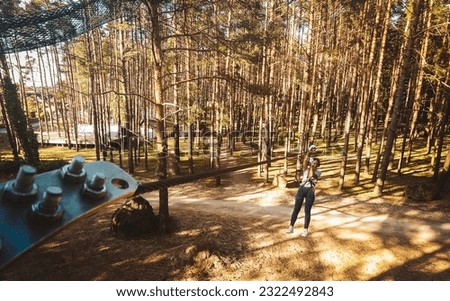 Palanga, Lithuania - 2023: young woman girl sliding along zipline in fir tree forest in summer. Lithuania adventure park in HBH.