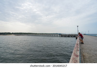 Palanga Lithuania - July 15 2021: Famous long pedestrian sea pier. Wooden bridge stretching into the sea. Young couple leaning on handrails and admiring views.