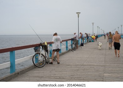 Palanga Lithuania - July 15 2021: Famous long pedestrian sea pier. Wooden bridge stretching into the sea. People handrails and admiring views. Teenage girl walking with her huge white and black dog.