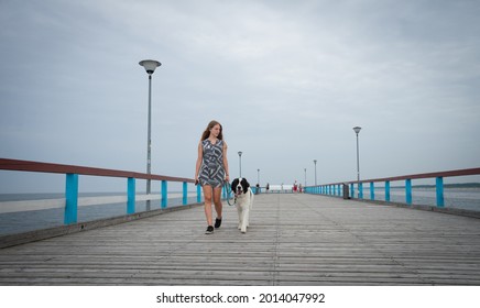Palanga Lithuania - July 15 2021: Famous long pedestrian sea pier. Wooden bridge stretching into the sea. Teenage Scandinavian blonde girl walking with her huge white and black dog.
