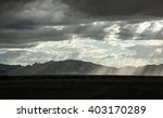 Pale beams of sunlight shine down to ground at late sunset from dark layer of cloud clumps/Wide White Sun Rays Shine Down onto Shadowed Earth from Grey Clumpy Layer of Clouds/Sun rays down to ground