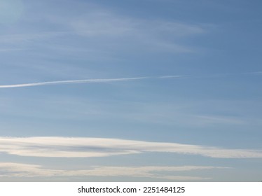 Pale blue sky with pale feathery and bright layered clouds above horizon. Contrail from plane. Gradient of color and illumination.

 - Powered by Shutterstock