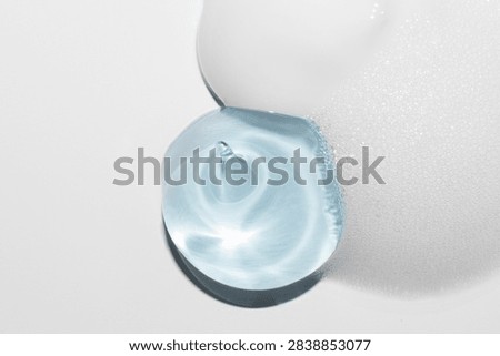 Pale blue translucent gel forms rounded shapes beside a white textured foam surface on a light background.