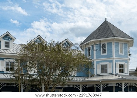 A pale blue wooden historic home with a rounds shaped turret. The large real estate property has small windows, white trim and wooden siding on the building. The multi-layered house is Victorian style