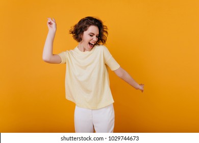 Gadis berambut coklat pucat dalam kaos kuning menari dengan ekspresi wajah yang terinspirasi. Wanita muda yang aktif dalam pakaian musim panas kasual bersenang-senang dalam ruangan.