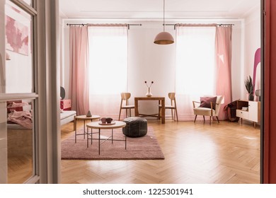 Pale pink living room interior in tenement house, real photo with copy space on the empty white wall and parquet on the floor