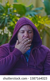 Pale Skinned Man In Violet Hoodie Is Smoking A Joint Cigarette. Close Up HDR Portrait, Bokeh.