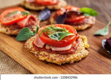 Paleo mini pizza with cauliflower crust, ham, tomatoes and basil on wooden cutting board
