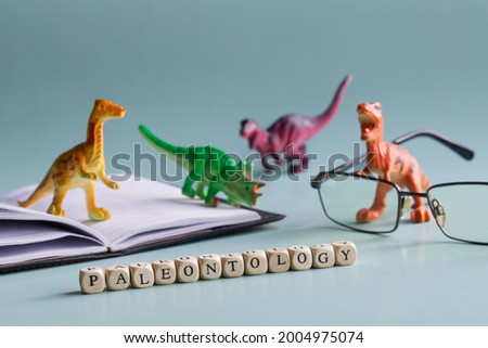 Paleontology inscription next to toy dinosaurs, open book or textbook and glasses. The concept of studying paleontology and dinosaurs in school, university and college. Pastel background