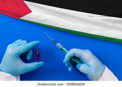 Palestine Vaccination. Hands Of Doctor Holding Syringe And Coronavirus (COVID-19) Vial Vaccine On Flag Palestine