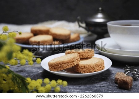 Palets bretons, french cookies. Shortbread Breton cookies, cup of tea and bouquet of mimosa on wooden dark background. Focus selective