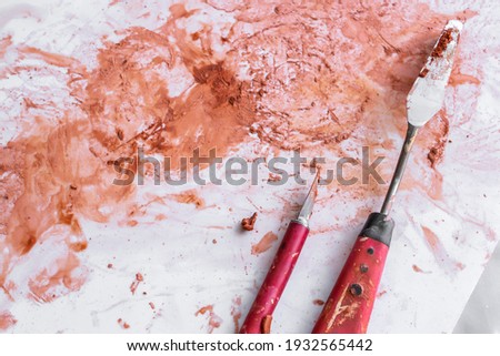 Palette knife and boxcutter knife laying on a white background splattered with Terracotta clay stains in an artist’s workshop in London, Ontario, Canada. 