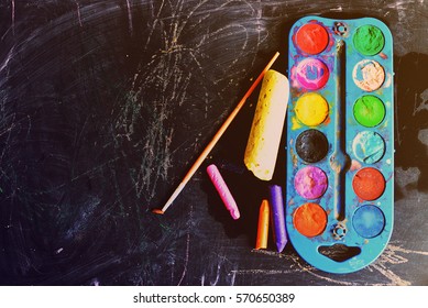 a palette of paints, chalk, pencils, paint on the plate against the background of a dirty school board. copy space