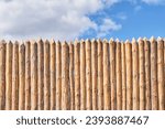 Palisade and cloudy sky as abstract rustic or historical background. Fence made of tightly driven stakes.