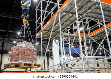 Pallet with cargo is hung on hook of crane. Mezzanine inside industrial building. Mechanism for lifting cargo in warehouse. Crane hook lifts heavy boxes. Warehouse enterprise. Lifting equipment - Powered by Shutterstock