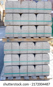 The pallet with a stack of concrete curbstone. Concrete curbs on wooden pallets stand on the street during street repair. gray concrete road pavement curb edge stone stacks on wooden pallets. pvc ties