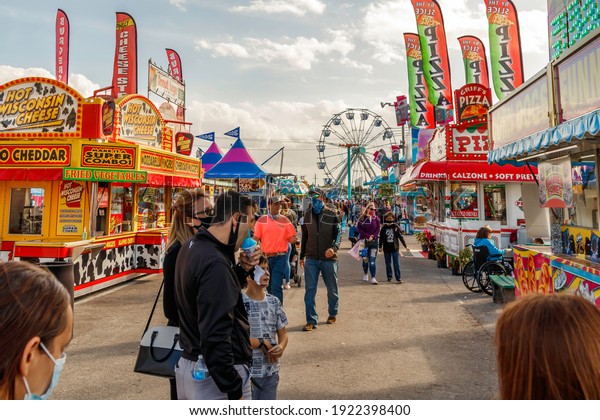 Palm Beach, Florida - USA - January 18, 2021 -\
The midway at the state and county fair with junk food vendors,\
amusement park games, ferris wheel, carnival rides and families\
enjoying the festival