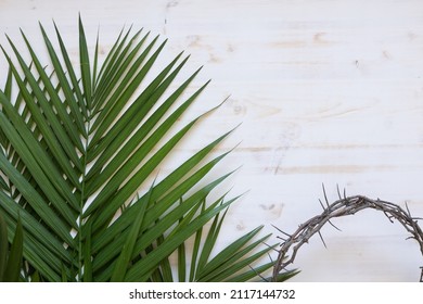 Palm fronds and partial crown of thorns on a white wood background with copy space - Shutterstock ID 2117144732