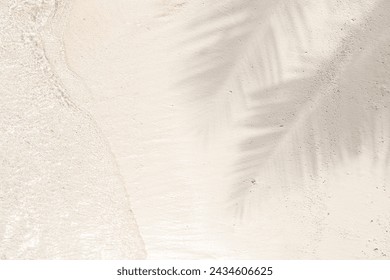 Palm leaf shadow on sand beach background with sun glitter on water surface