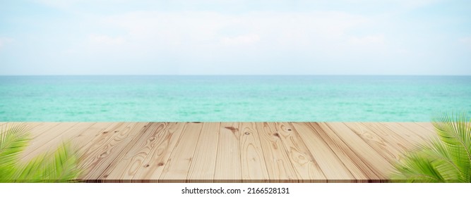 Palm Leaves With Wooden On Sea.blank Table On Blue Water Shore And Blue Sky At Coast. Sunlight Blur Bokeh On Ocean. Mockup Tropical Seaside. Tourism Relax Vacation Travel Summer Holidays.