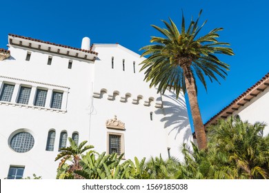 A Palm Tree And A Historic White Spanish Colonial Revival Architecture Style Building With Ornate Windows And Trim In Santa Barbara, California, USA