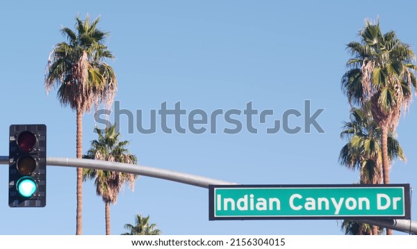 Palm trees and blue sky, Palm Springs resort city\
near Los Angeles, street road sign, semaphore traffic lights on\
crossroad. California desert valley summer road trip on car, travel\
USA. Indian Canyon
