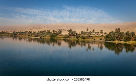 Palmiers et verdure se reflétant sur le Nil avec des montagnes en arrière-plan